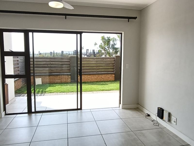 Bright and spacious living area featuring large sliding glass doors that open onto a private patio and garden, finished with neutral floor tiles.