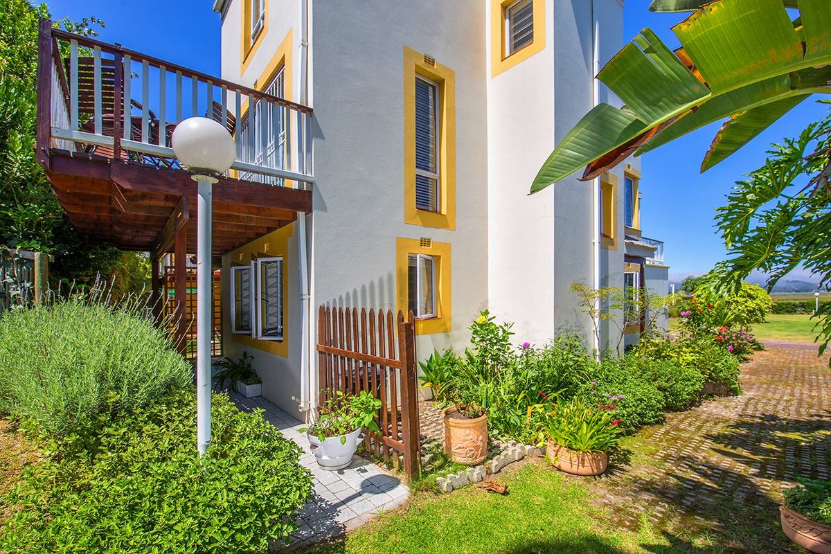 Rear exterior view of the townhouse featuring a raised wooden balcony, paved garden path, and established landscaping.