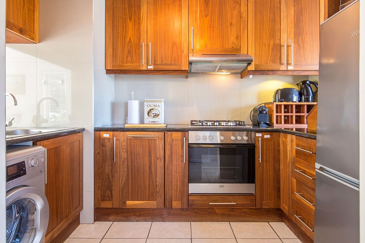 A well-maintained kitchen featuring warm wooden cabinetry, granite countertops, a built-in oven with gas hob, and integrated laundry plumbing.