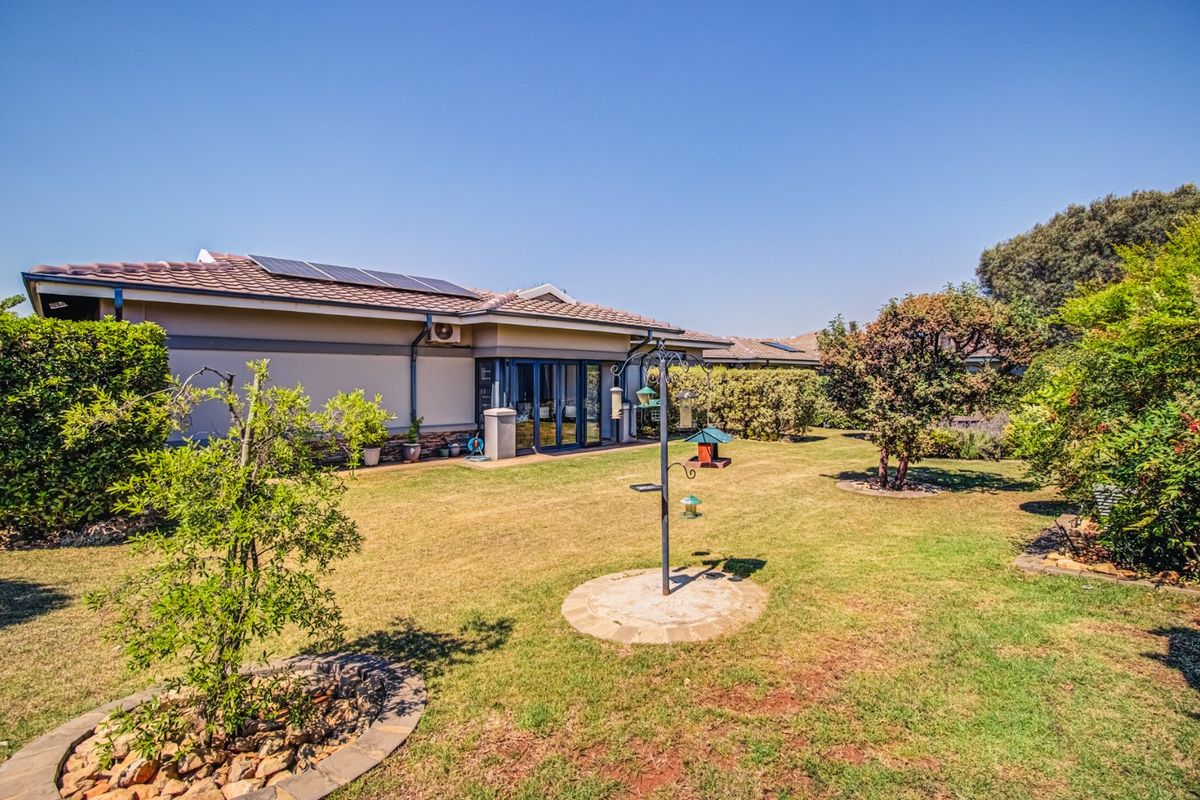 Rear view of the house featuring a well-maintained lawn, solar panels on the tiled roof, and large sliding glass doors leading to the interior.
