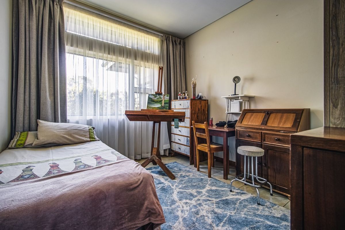 A functional bedroom featuring large windows with natural light, tiled flooring, and neutral wall finishes, suitable for a guest room or home office.