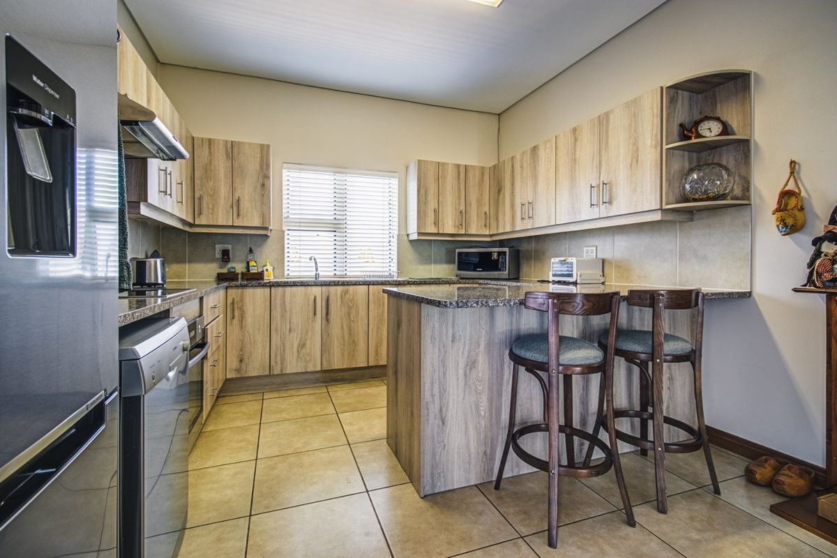 A functional kitchen featuring light wood-grain cabinetry, granite countertops, a breakfast bar, and tiled flooring with ample storage space.