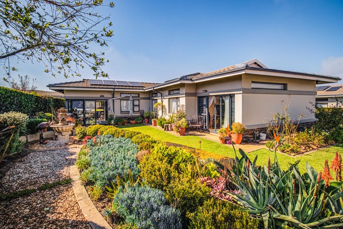 Rear view of a well-maintained single-story house featuring solar panels, stone cladding accents, and a beautifully landscaped garden with a paved walkway.