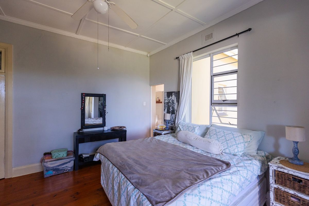 A bedroom featuring original timber flooring, a ceiling fan, and an en-suite bathroom access point, providing a functional and classic living space.