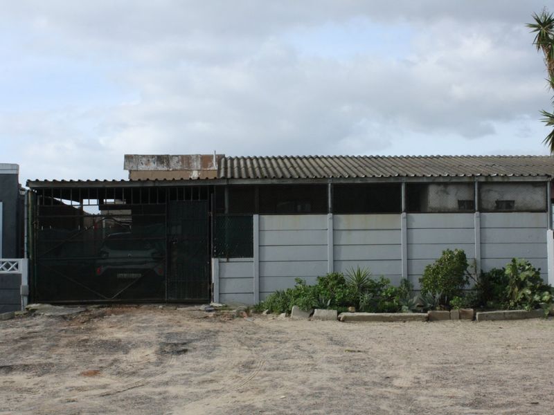 Front exterior view of the property featuring a corrugated roof, precast concrete boundary wall, and gated driveway access.