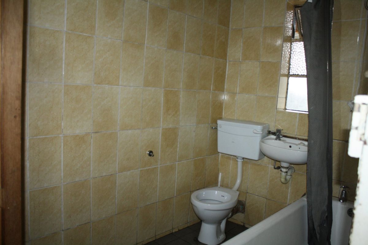 A dated bathroom featuring original ceramic wall tiles, a standard toilet, wall-mounted basin, and a bathtub with an obscured glass window.