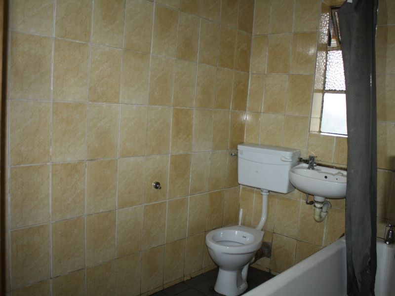 A dated bathroom featuring original ceramic wall tiles, a standard toilet, wall-mounted basin, and a bathtub with an obscured glass window.