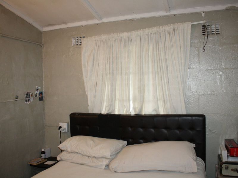 A bedroom featuring painted block walls, ceiling panels, and integrated air vents, requiring cosmetic updates to improve the overall finish and condition.