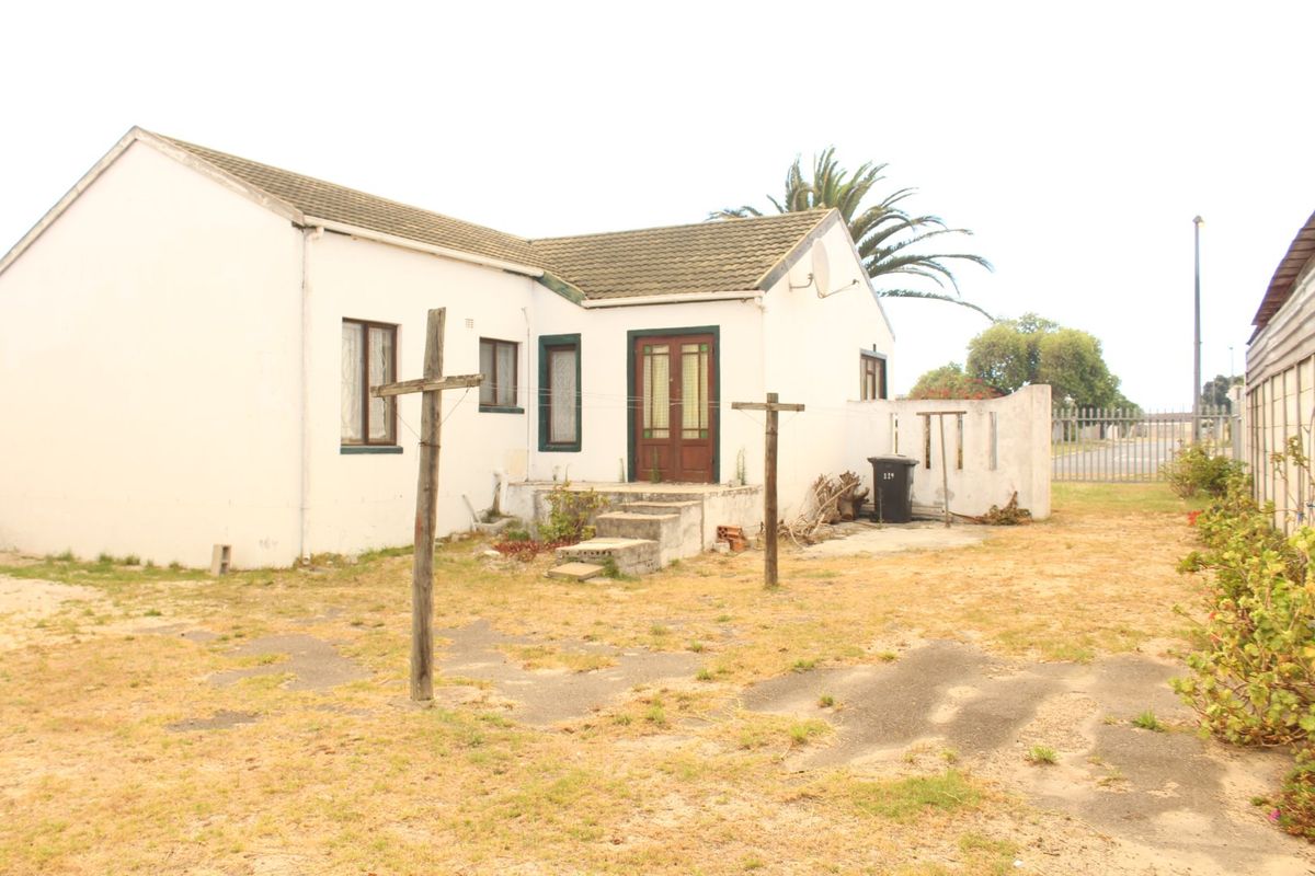 Rear view of a detached house featuring a tiled roof, timber entrance door, and concrete steps leading to a large, unmaintained garden area.