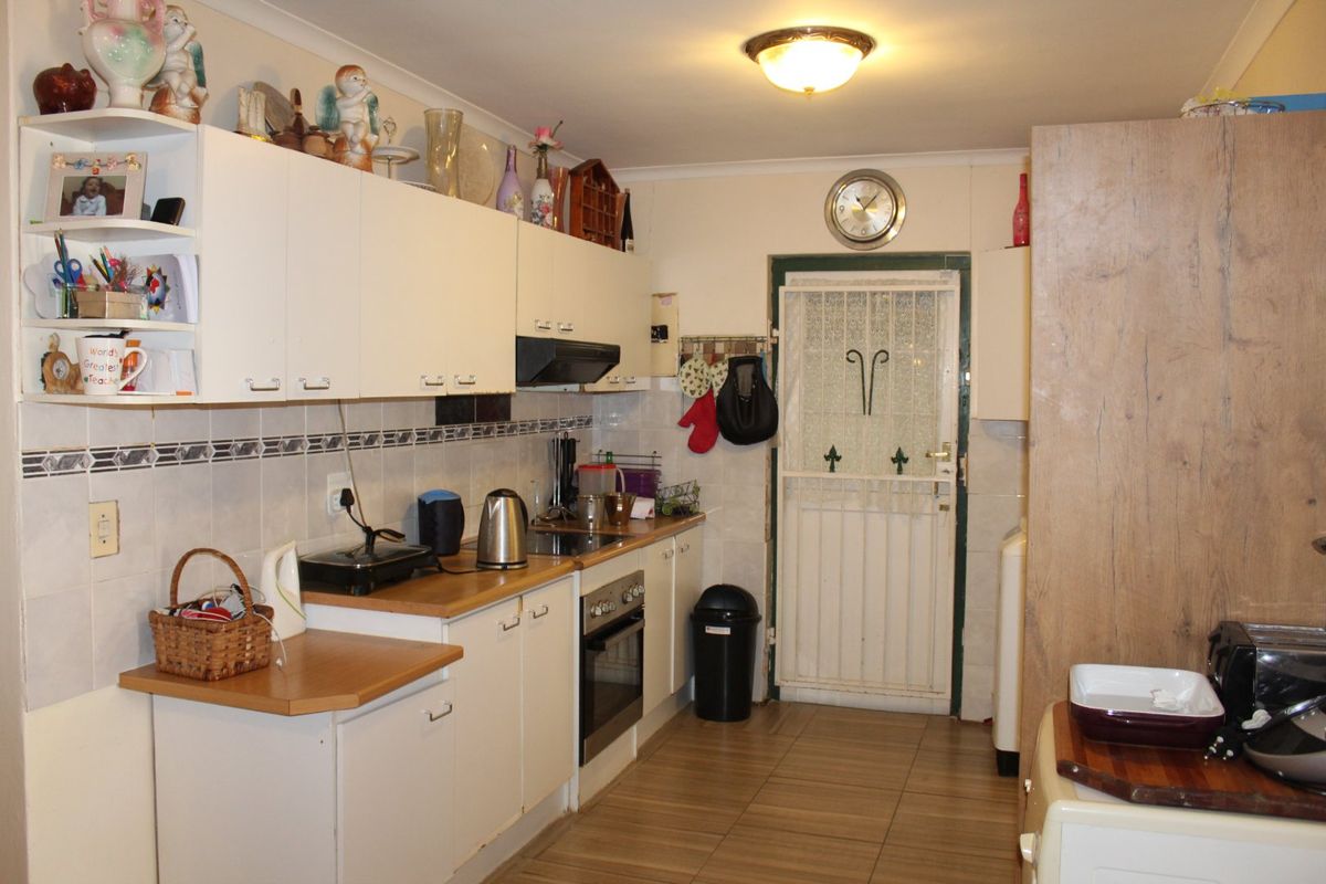 A functional kitchen featuring built-in cabinetry, an integrated oven and hob, tiled splashbacks, and direct access to the exterior via a security gate.