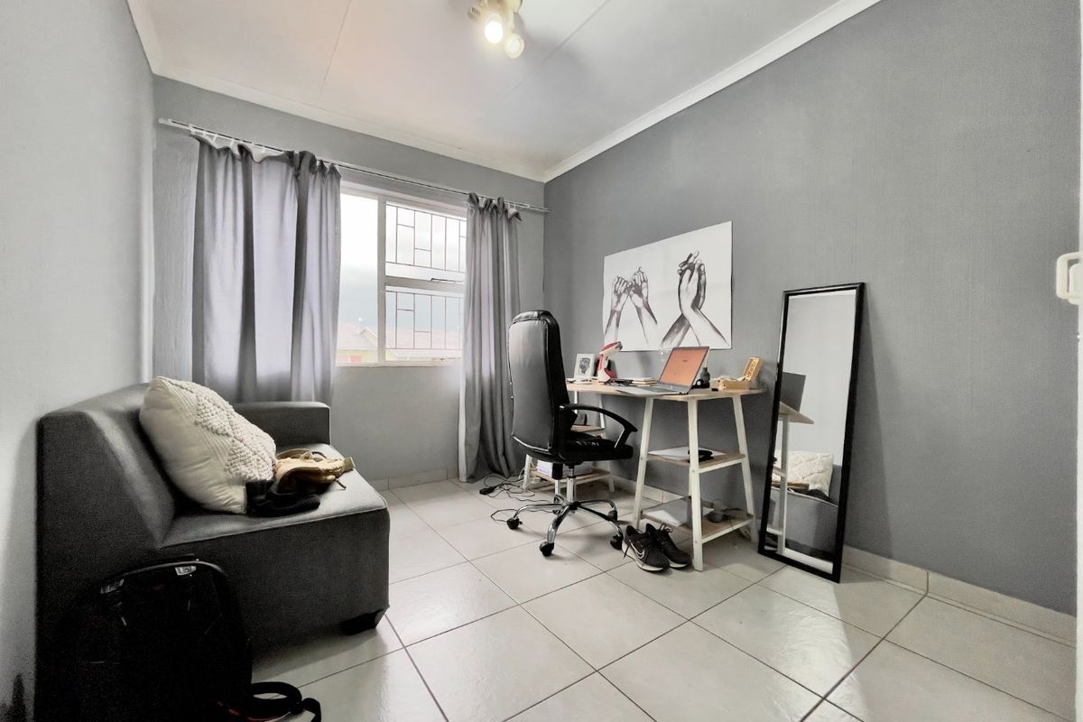 A functional bedroom or home office space featuring neutral tiled flooring, a window with security bars, and simple coved cornicing.