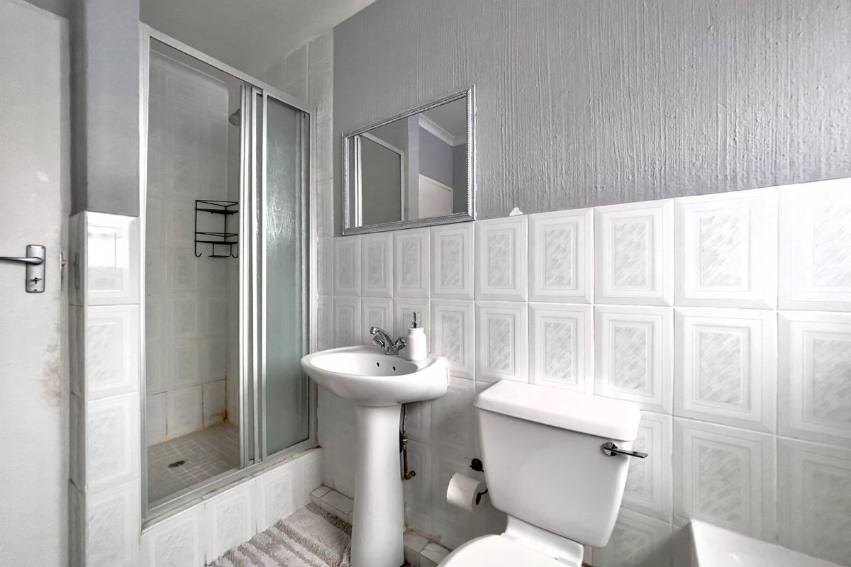 A functional bathroom featuring a pedestal basin, toilet, and a glass-enclosed shower with tiled wall finishes.