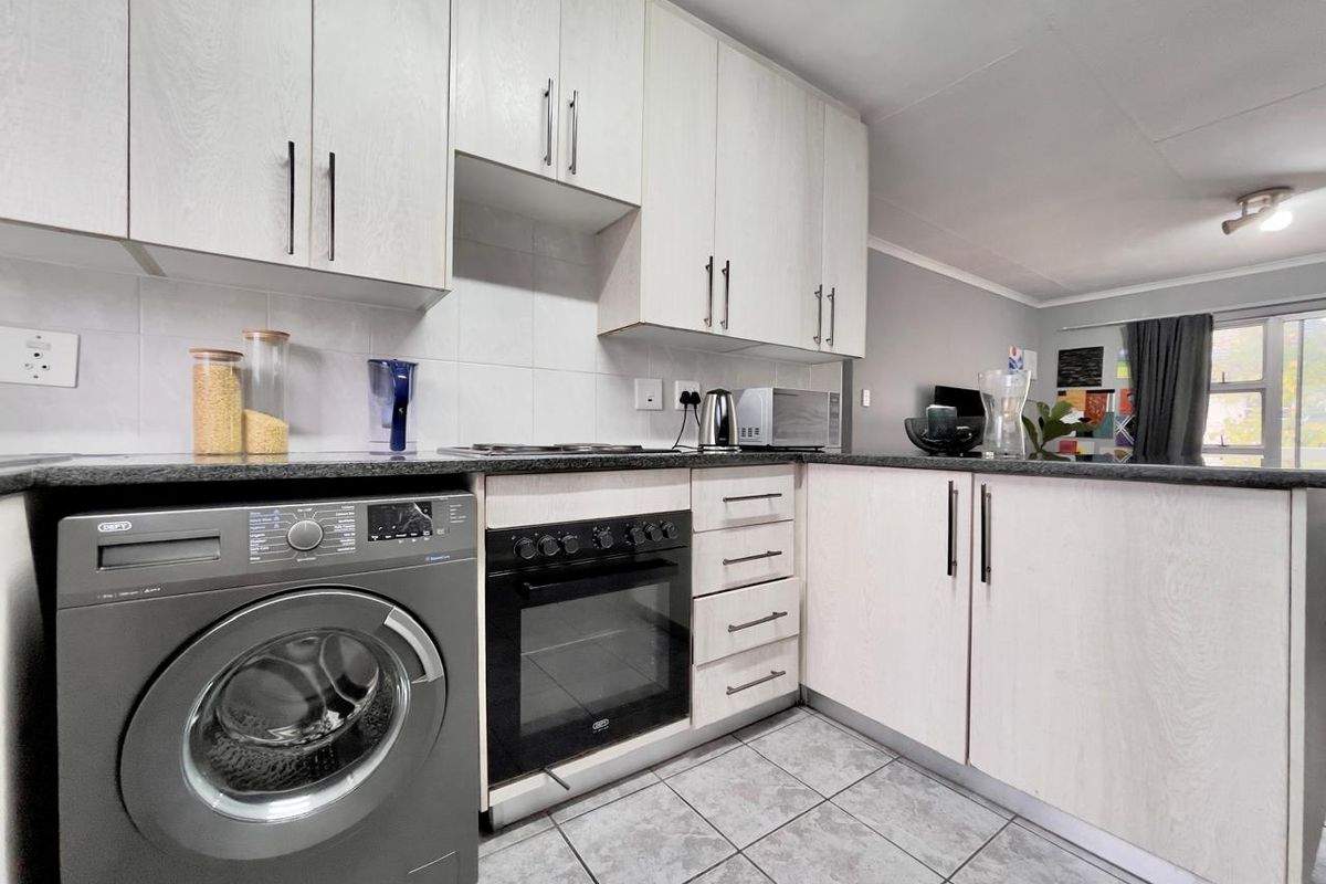 A functional kitchen featuring light wood-grain cabinetry, dark laminate countertops, a built-in oven, and tiled flooring, with an integrated laundry appliance space.