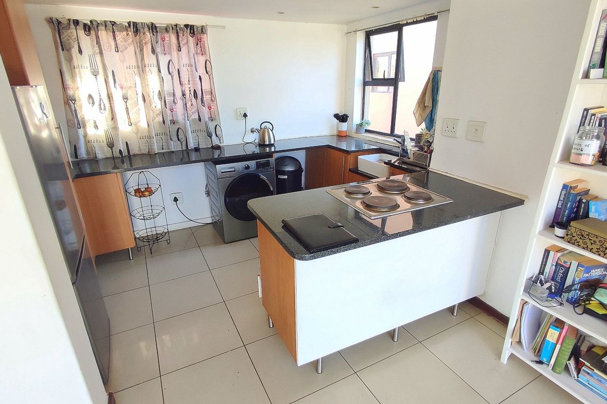 Compact kitchen featuring granite countertops, a built-in electric hob, ceramic floor tiles, and integrated cabinetry with space for laundry appliances.