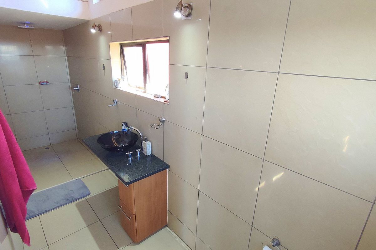 A modern bathroom featuring floor-to-ceiling beige tiling, a floating vanity with a dark stone countertop, and a walk-in shower area.