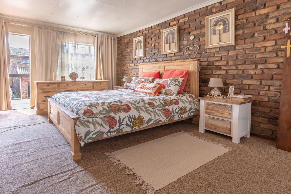 Spacious bedroom featuring a rustic exposed brick feature wall, carpeted flooring, and direct access to a private balcony.