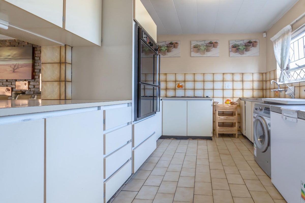 A functional kitchen featuring built-in cabinetry, a wall-mounted oven, tiled flooring, and a dedicated space for laundry appliances.