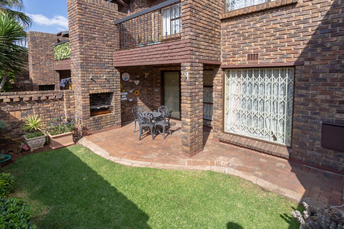 A private rear patio area featuring a built-in brick braai, paved flooring, and direct access to a small, well-maintained garden space.
