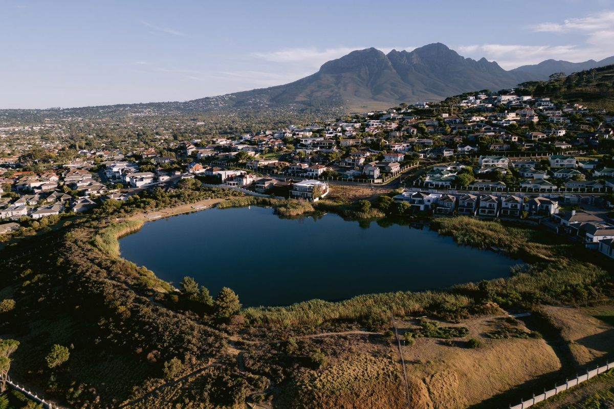 An aerial view of a residential estate featuring a central lake with scenic mountain views in the background.