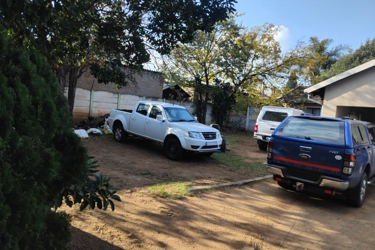 A rear exterior view of the property featuring a large unpaved yard area, boundary wall, and paved driveway section.