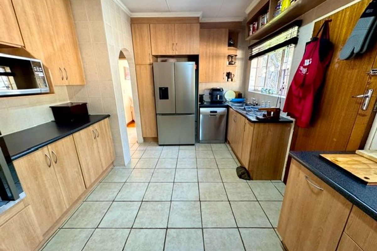 A functional kitchen featuring laminate cabinetry, tiled flooring, and built-in appliances, offering a practical layout with potential for modern cosmetic updates.