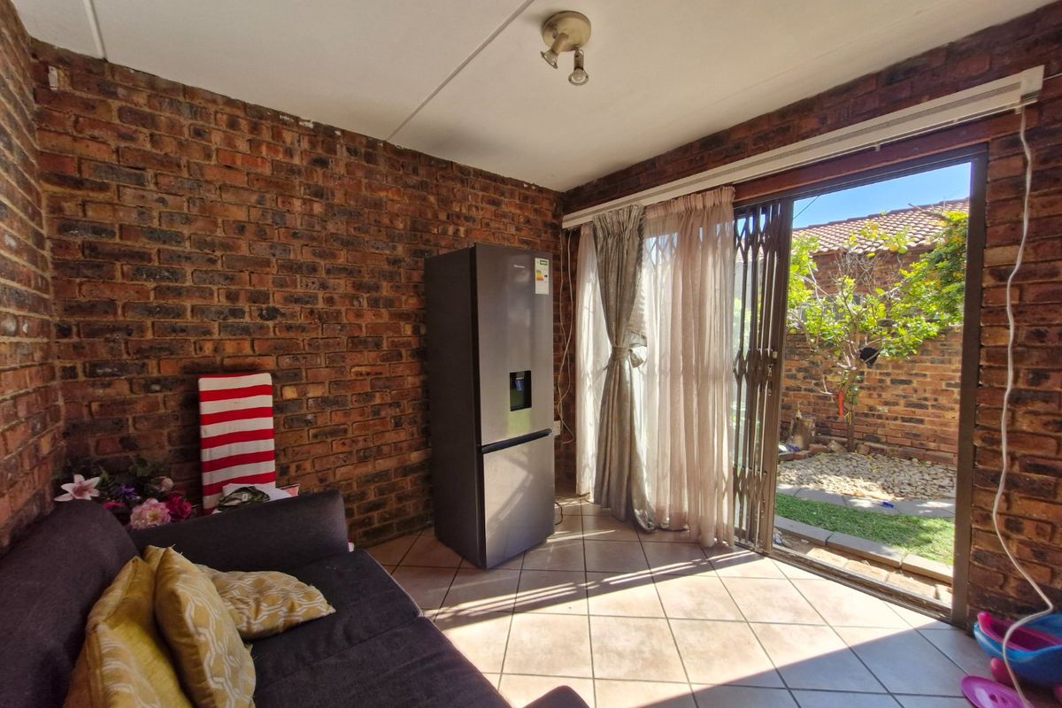 Living room featuring exposed brick walls, ceramic floor tiles, and a sliding glass door providing direct access to the rear garden area.