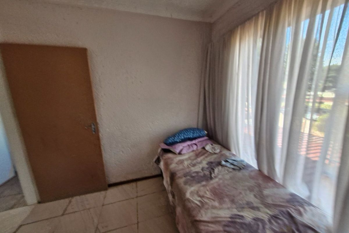 A bedroom featuring tiled flooring, textured walls, and a large window with curtains, offering a functional space in need of cosmetic updates.