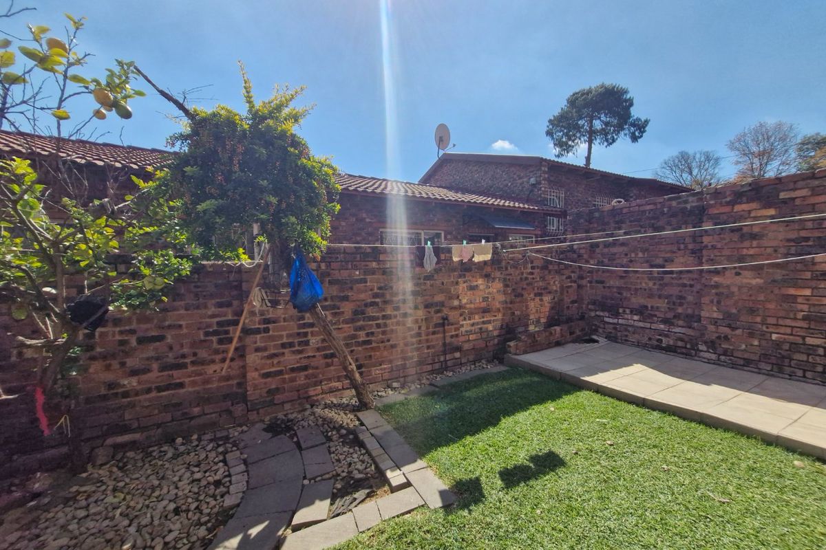 A private rear garden featuring a brick boundary wall, a small lawn, and a paved patio area.