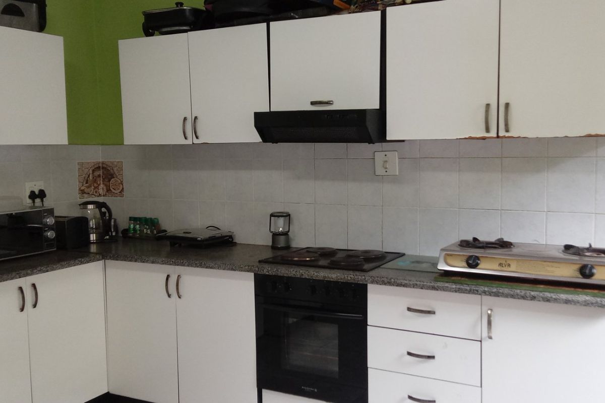 A functional kitchen featuring white cabinetry, laminate countertops, tiled backsplash, and built-in oven with extractor fan, requiring some cosmetic updates.