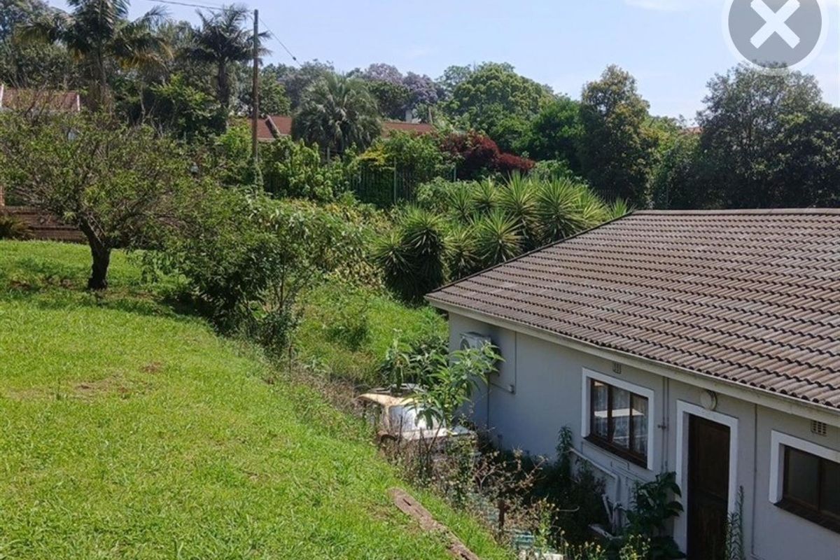 Rear view of the property showing the tiled roof, exterior wall, and surrounding sloped garden area.