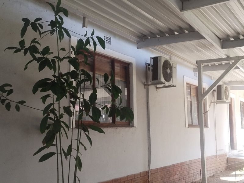 A covered outdoor patio area featuring a corrugated metal roof, brick base detailing, and wall-mounted air conditioning units.