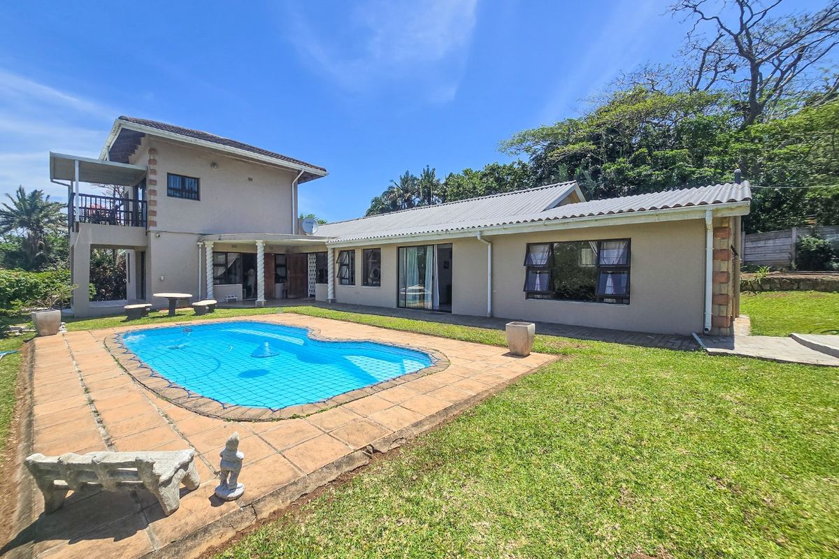 Rear view of the house featuring a swimming pool, paved pool deck, covered patio area, and an upper-level balcony.