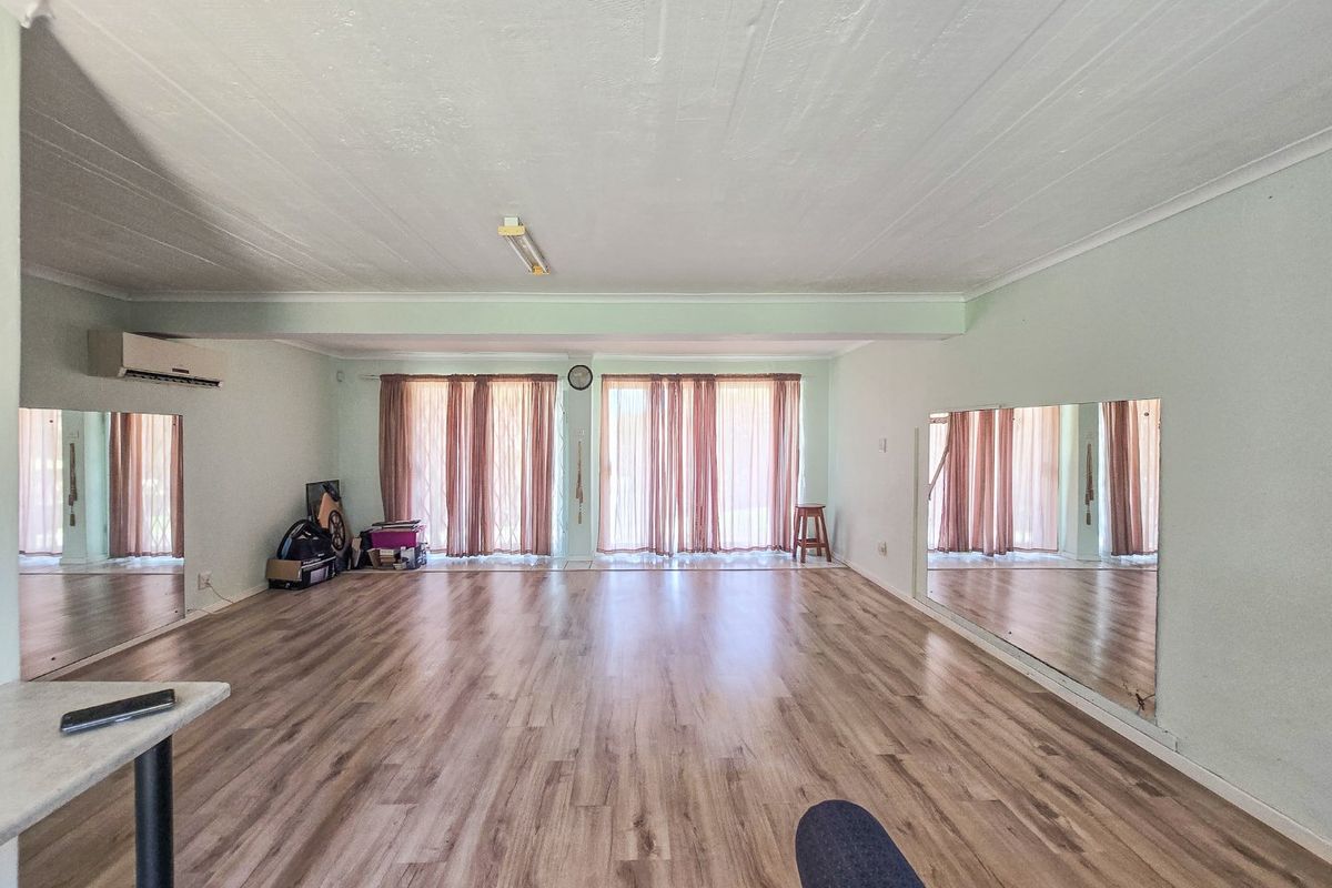 Spacious living area featuring laminate flooring, wall-mounted air conditioning, and large mirrors, offering a versatile open space with natural light through sliding glass doors.