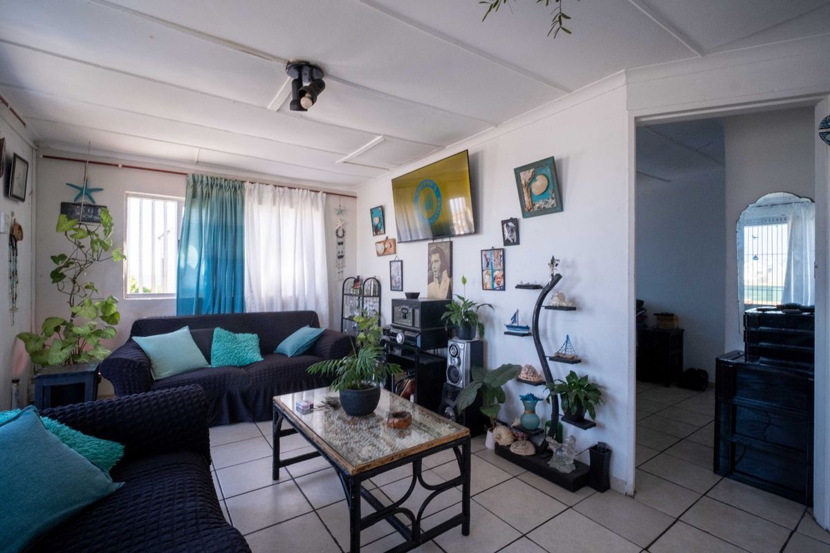 A living room featuring tiled flooring, ceiling panels, and a window with security bars, offering a functional space for relaxation.