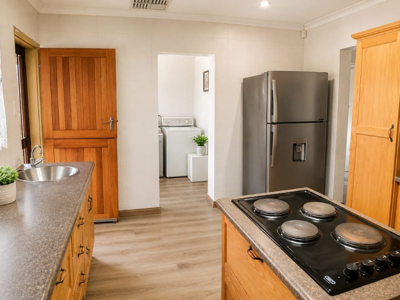 A functional kitchen featuring timber cabinetry, laminate countertops, an integrated electric cooktop, and direct access to a separate laundry area.