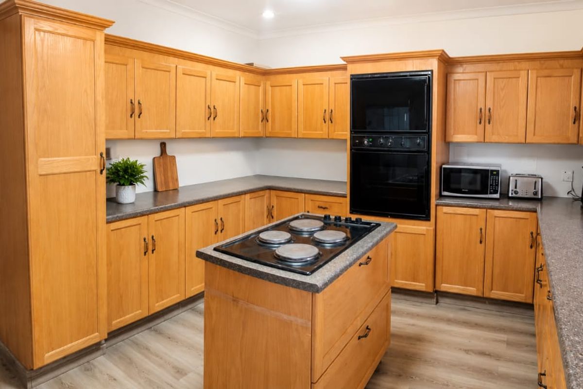 A spacious kitchen featuring traditional oak cabinetry, laminate countertops, a central island with an electric cooktop, and a built-in double oven.