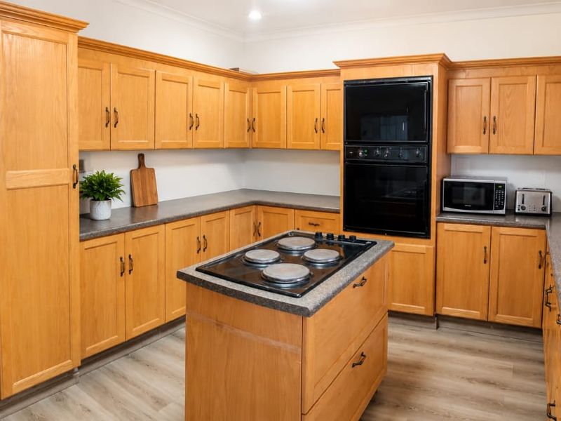 A spacious kitchen featuring traditional oak cabinetry, laminate countertops, a central island with an electric cooktop, and a built-in double oven.