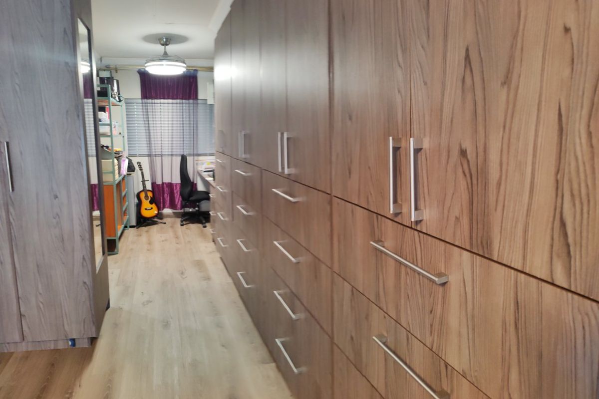 A bedroom featuring extensive floor-to-ceiling built-in cabinetry with wood-grain finish and modern laminate flooring.