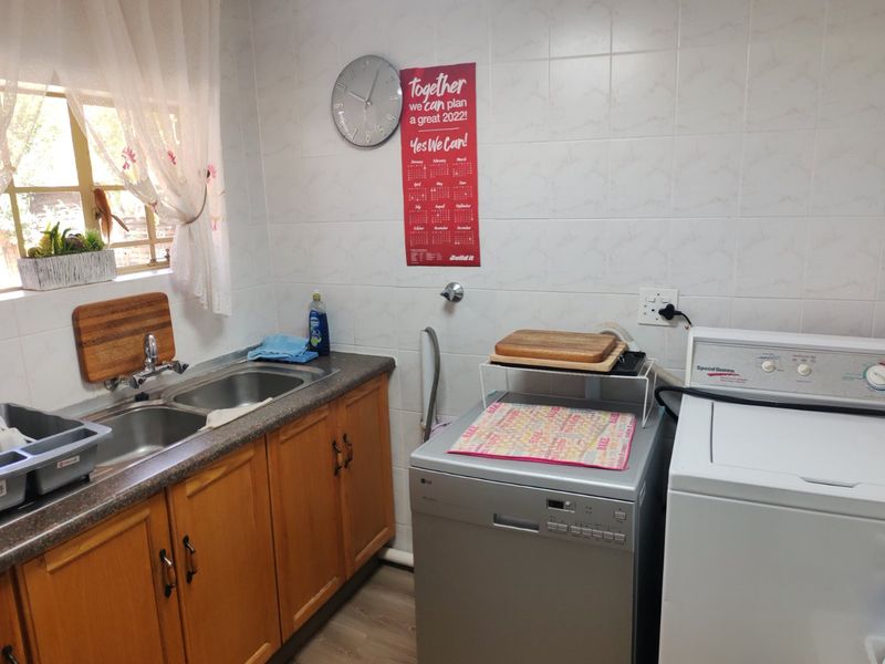 Functional laundry room featuring a double basin stainless steel sink, tiled splashback, and ample laminate cabinetry for storage and utility needs.