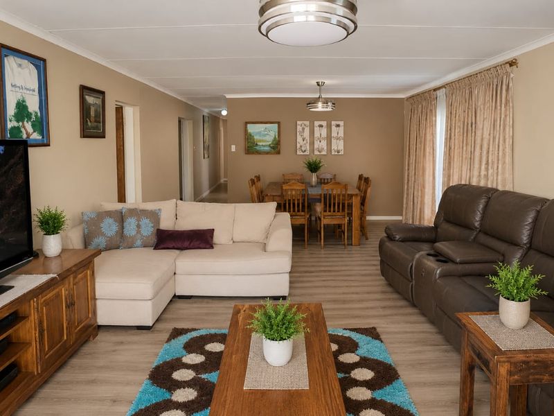 Spacious open-plan living and dining area featuring neutral wall tones, modern laminate flooring, and natural light through sliding glass doors.