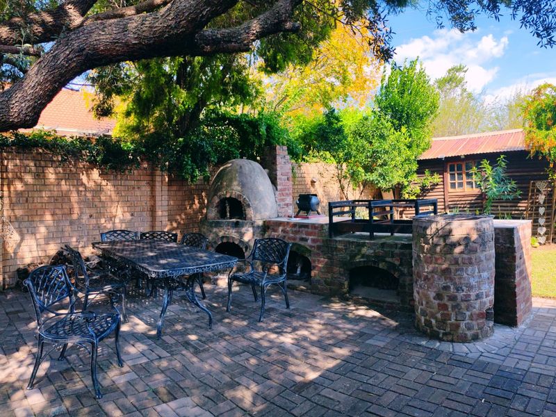 Outdoor entertainment area featuring a built-in brick braai and traditional pizza oven, set on a paved patio within a private garden.