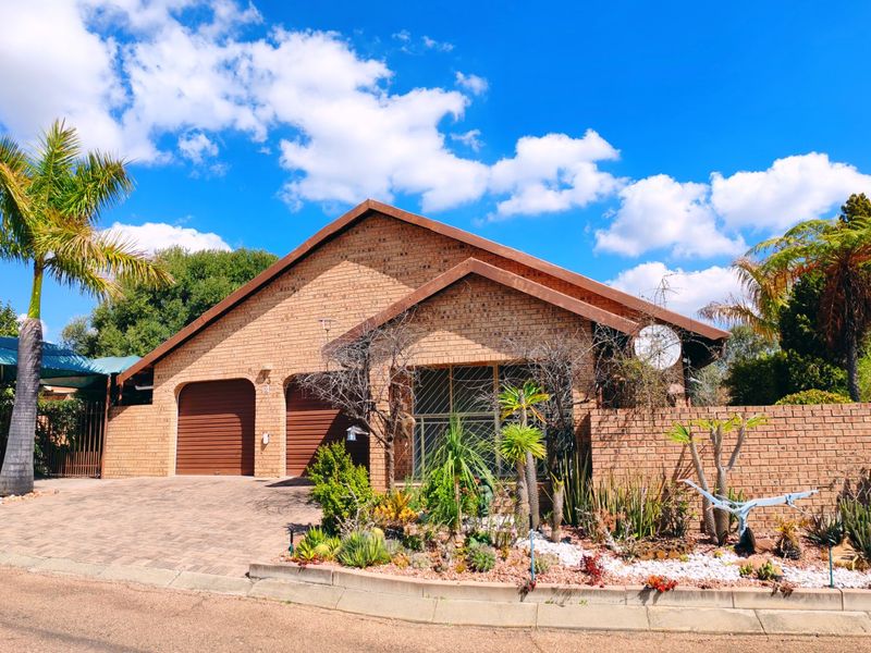 Front view of a brick-faced house featuring a double garage, paved driveway, and established garden with a carport.