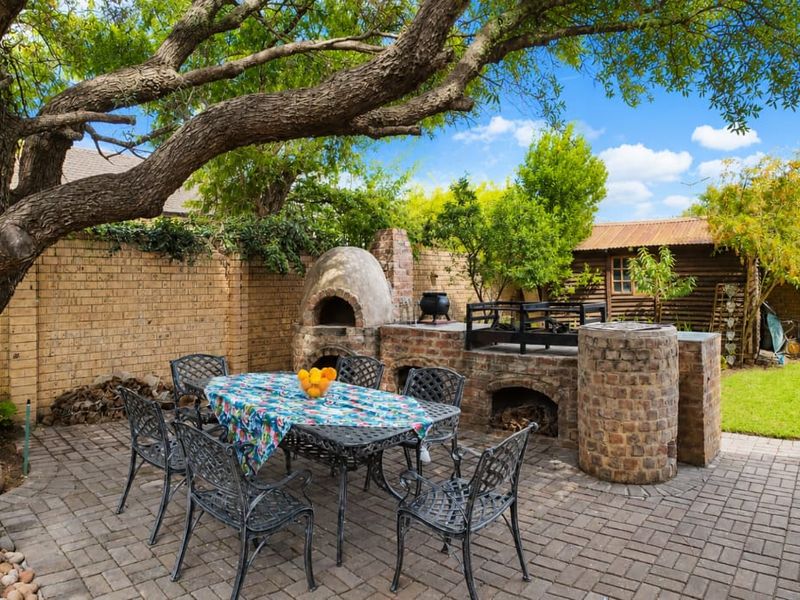 Outdoor entertainment area featuring a paved patio, built-in brick braai, and a traditional pizza oven, set within a private garden space.