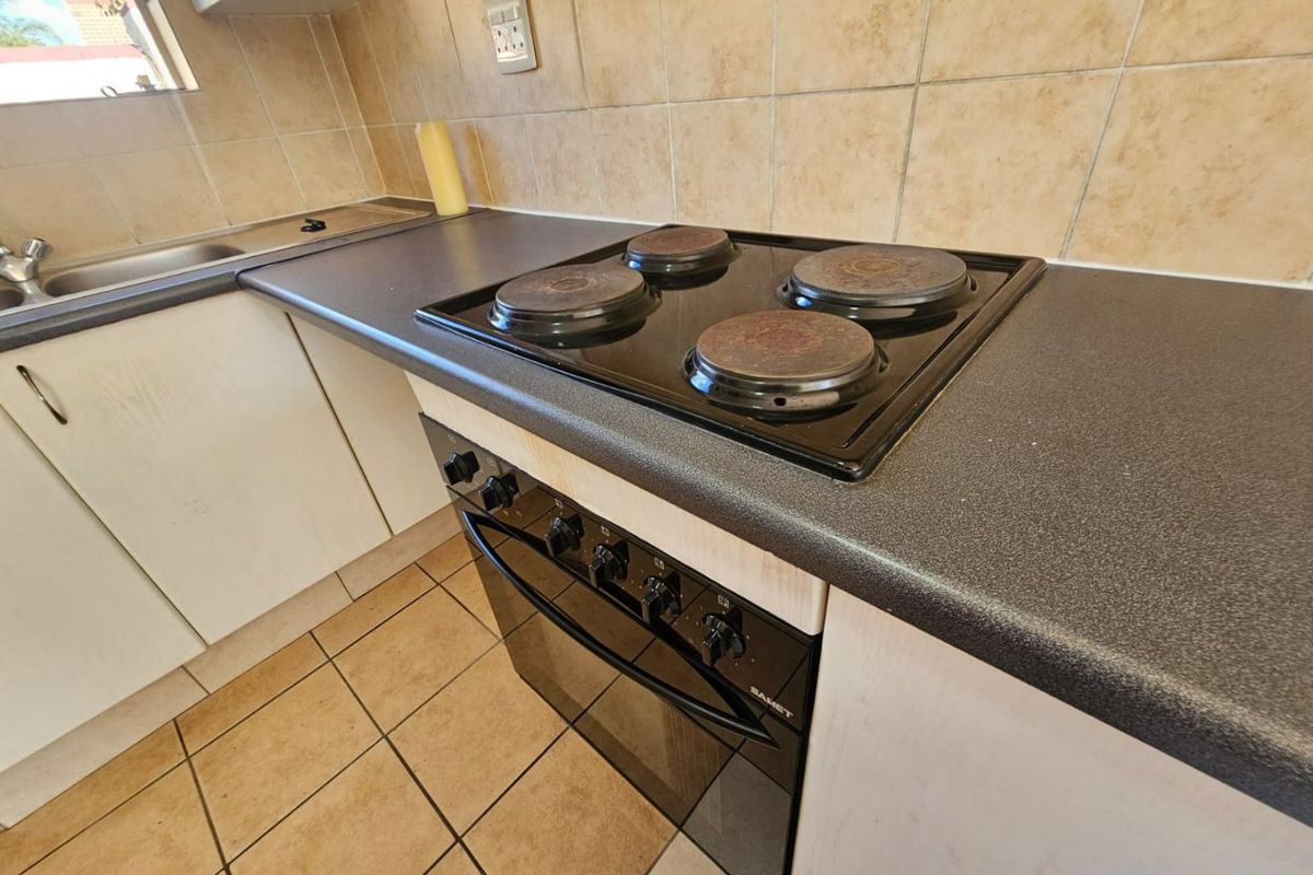 A functional kitchen area featuring a built-in oven and electric hob, tiled backsplash, and laminate countertops with integrated sink.
