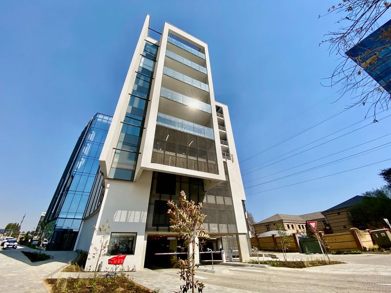 Modern multi-story commercial building featuring a glass facade, integrated balconies, and a secure ground-level parking entrance.