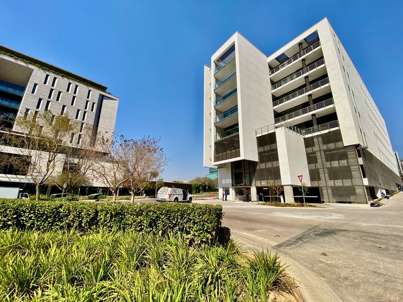Modern commercial building exterior featuring clean white facade, glass balconies, and paved driveway access within a professional office park setting.