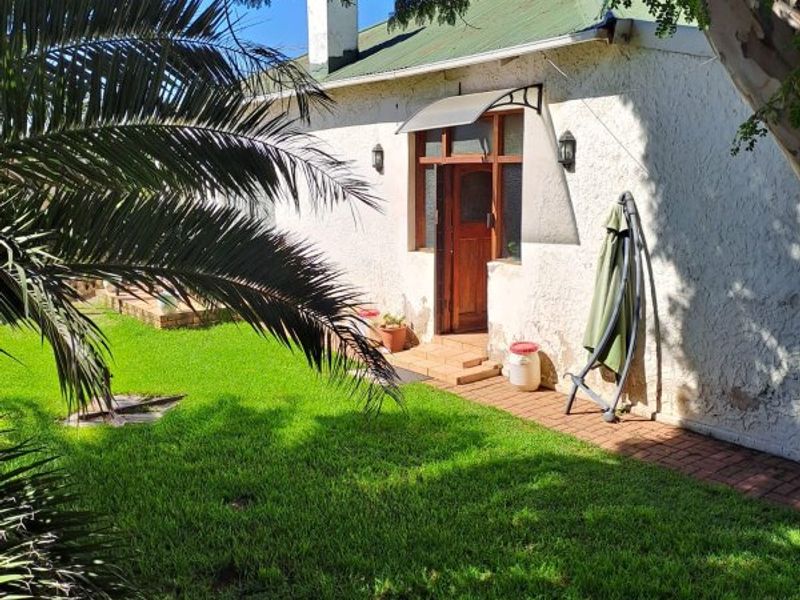Rear view of the property featuring a green pitched roof, brick pathway, and established garden area with mature trees.