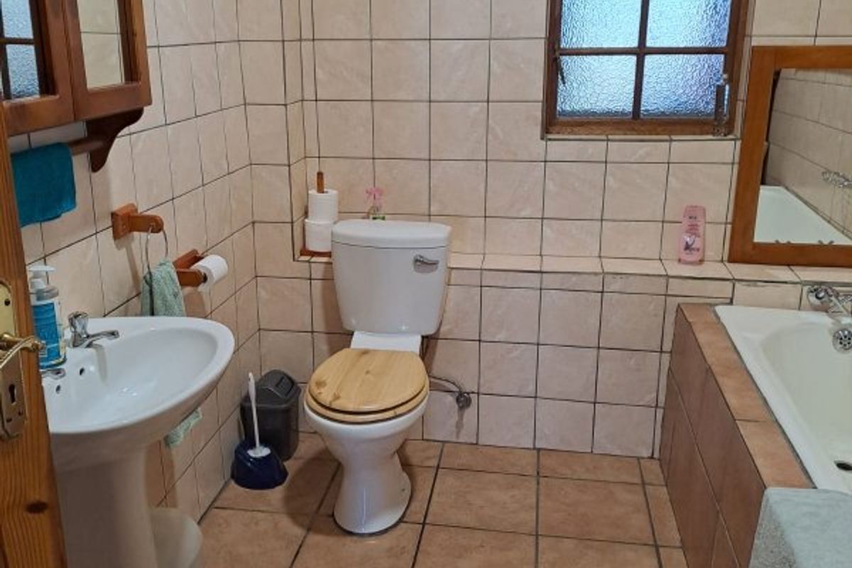 A functional bathroom featuring a pedestal basin, toilet, and built-in bathtub with classic tiled finishes and a timber-framed window.