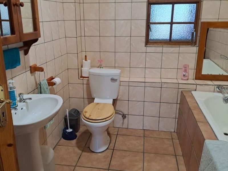 A functional bathroom featuring a pedestal basin, toilet, and built-in bathtub with classic tiled finishes and a timber-framed window.