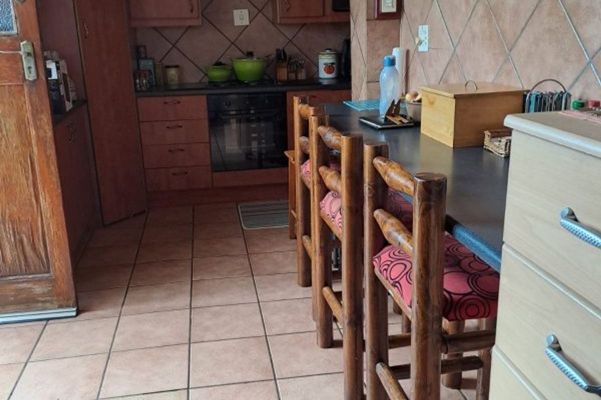 A functional kitchen featuring wooden cabinetry, a built-in oven with hob, tiled flooring, and a breakfast bar area.